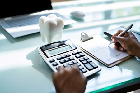 Tooth and calculator on desk representing cost of emergency dentist in Fort Worth, TX