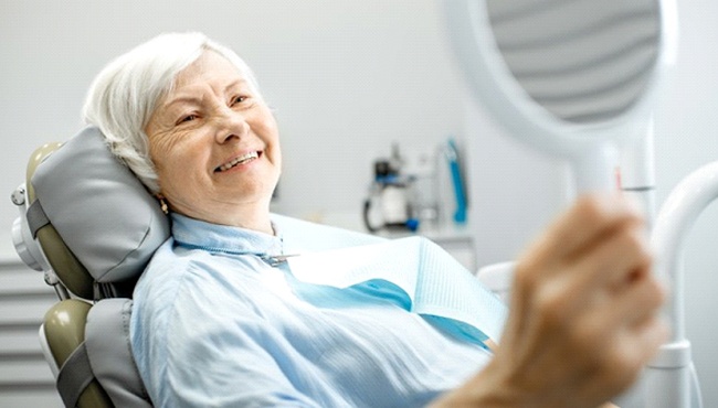 older woman using hand mirror to admire her dental implants in Ft. Worth 