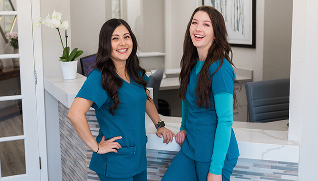 Two smiling dental team members at front desk