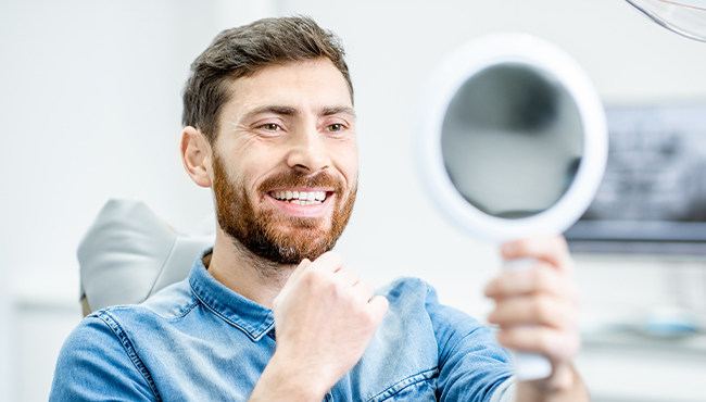Man looking at smile in mirror after metal free dental restoration