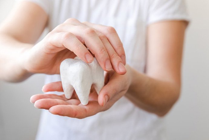 Person holding a giant plaster model of a tooth protectively 