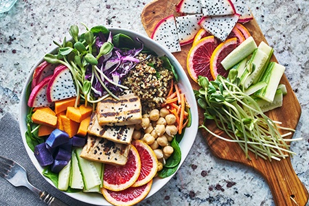 a bowl of salad with a board of fresh vegetables next to it