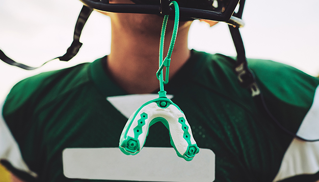 Teen boy with green sports mouthguard hanging from football helmet