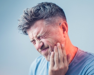 Man in need of restorative dentistry holding his cheek in pain
