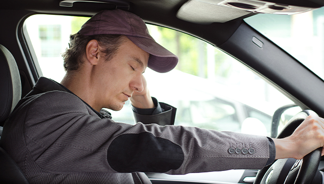 Exhausted man in need of sleep apnea treatment falling asleep while driving