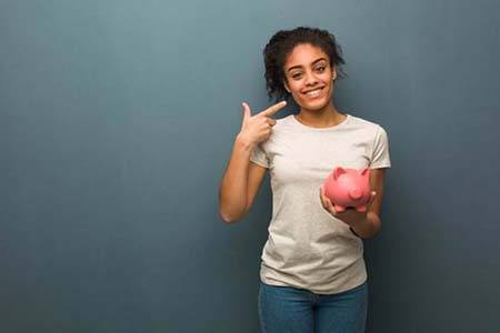 woman holding piggy bank and pointing to teeth
