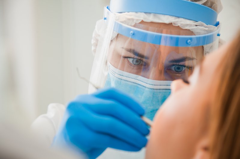 a dental staff member wearing personal protective equipment and performing a regular checkup and cleaning on a patient