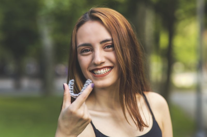 Woman smiling while holding Invisalign tray