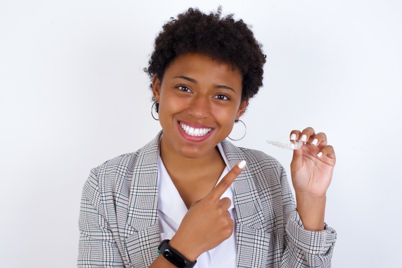 person pointing to Invisalign aligner and smiling